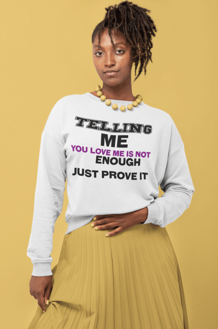 A woman wearing a white sweatshirt with the words " telling me you love me is not enough just prove it ".
