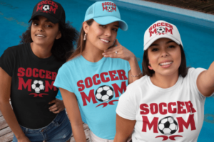 Three women wearing hats and shirts with soccer mom on them.