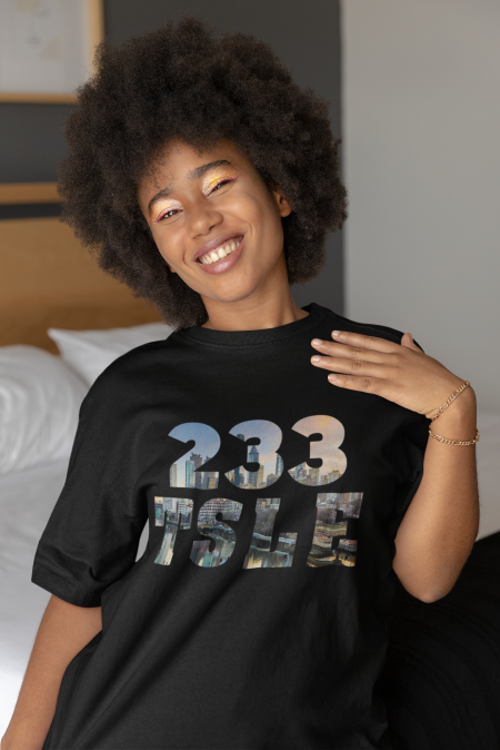 A woman standing in front of a bed wearing a t-shirt.