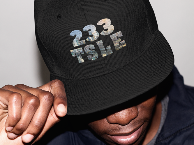 A man wearing a black hat with the words " 2 3 3 tsle ".